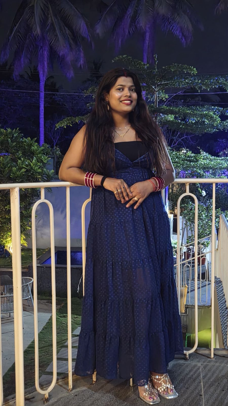 Nishtha after breast reduction - front view in navy blue dress at a night event with palm trees and purple lighting