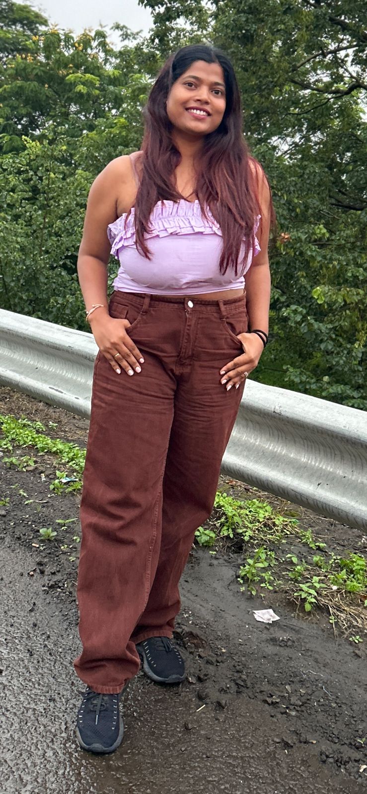 Nishtha before breast reduction - front view in pink ruffled top and brown jeans, outdoors